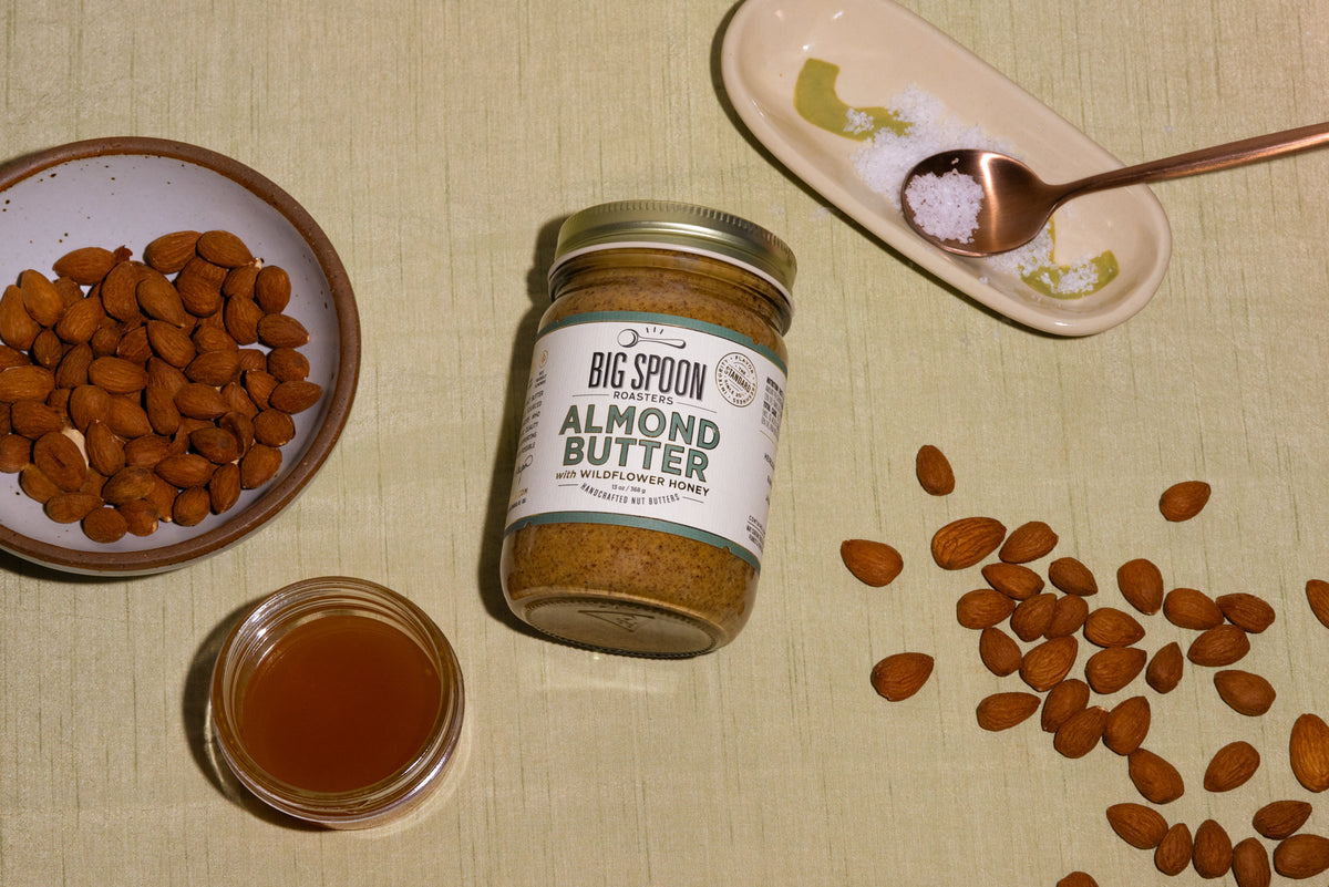 a jar of Almond Butter surrounded by a bowl of almonds, a jar of honey, sea salt, and other almonds