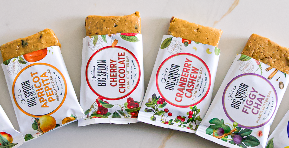 Four Big Spoon Roasters snack bars with colorful packaging on a marble surface.