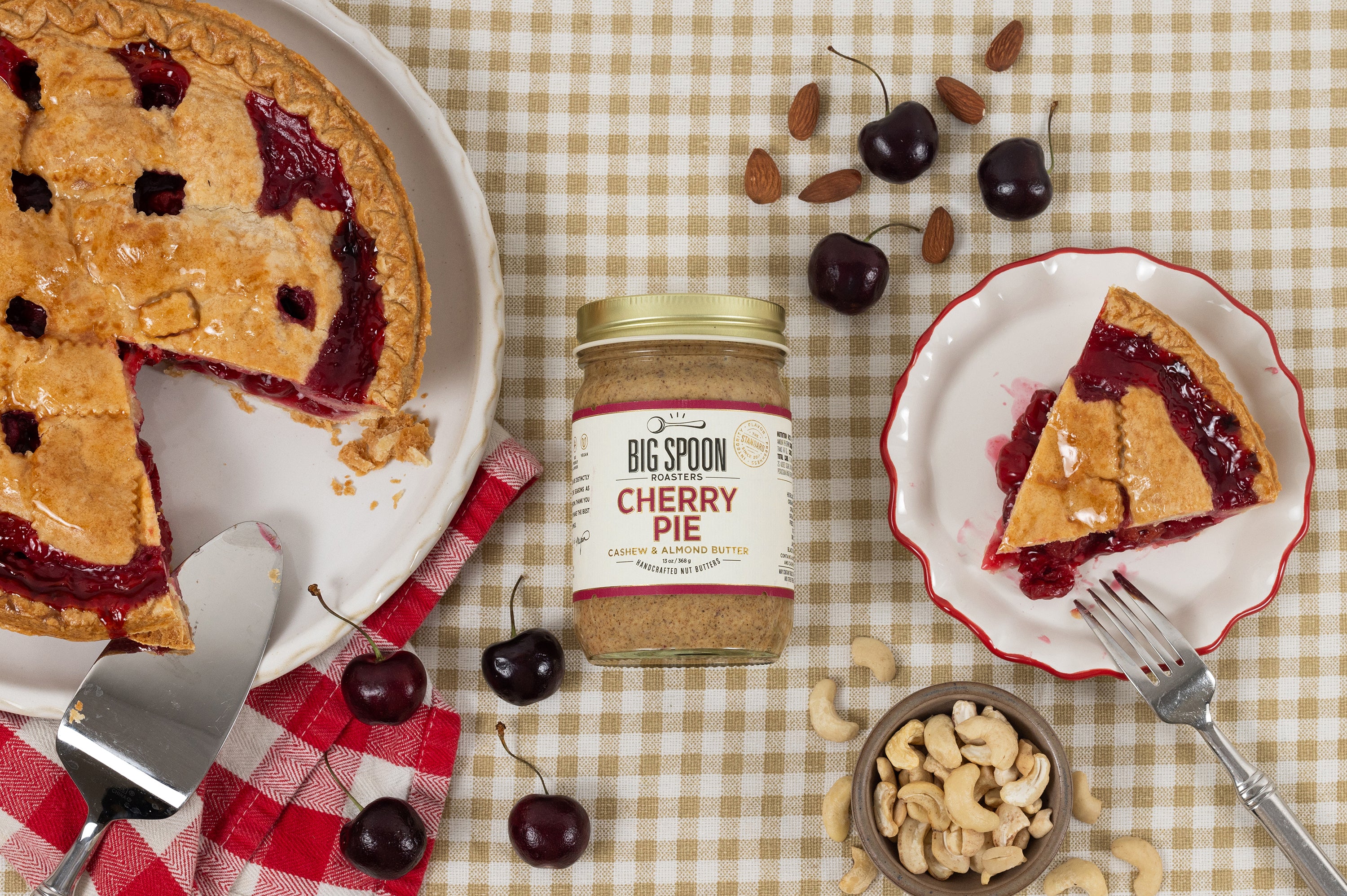 Jar of cherry pie nut butter surrounded by cherry pie, cherries, and nuts