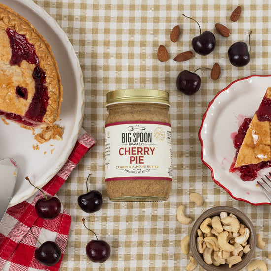 Jar of cherry pie nut butter surrounded by cherry pie, cherries, and nuts