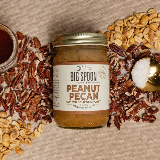 Jar of Big Spoon Roasters Peanut Pecan spread with ingredients and a spoon on a beige background